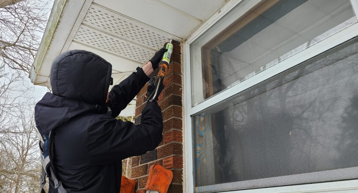 A Skedaddle technician in a full white hazmat suit and respirator using a fogging machine to sanitize an attic space after a wildlife infestation.