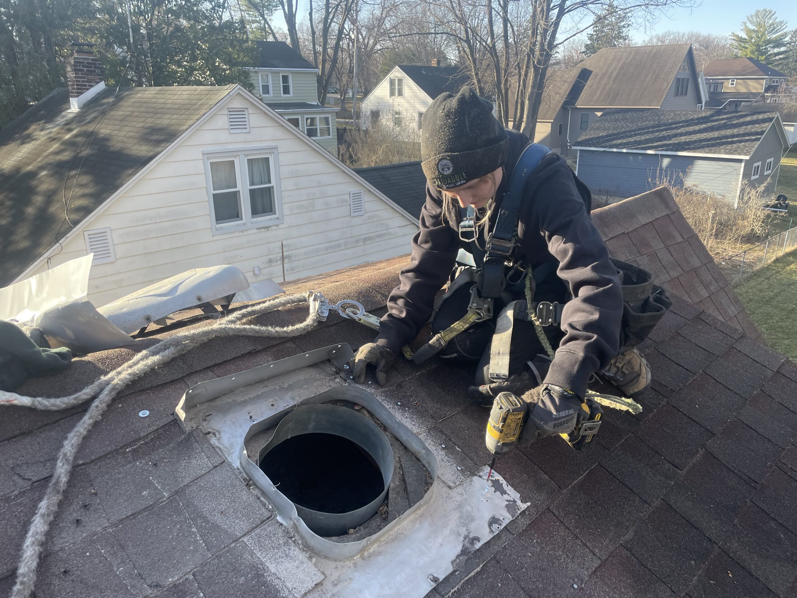 Skedaddle technician using a power drill to secure a chimney vent cover on a shingled roof.