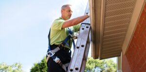 A Skedaddle technician wearing a safety harness climbs a ladder to inspect a home's soffit and gutters for squirrel entry points.