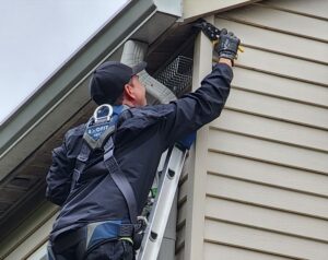 Skedaddle technician in branded gear working on a tall ladder to secure a roofline in Baltimore.