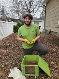 A Skedaddle technician in a green uniform gently holding a tiny baby squirrel in a gloved hand during a residential rescue.