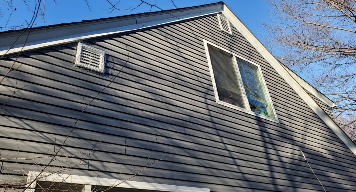 Two white square exterior wall vents on a gray-sided house, both secured with heavy-duty galvanized steel mesh covers.