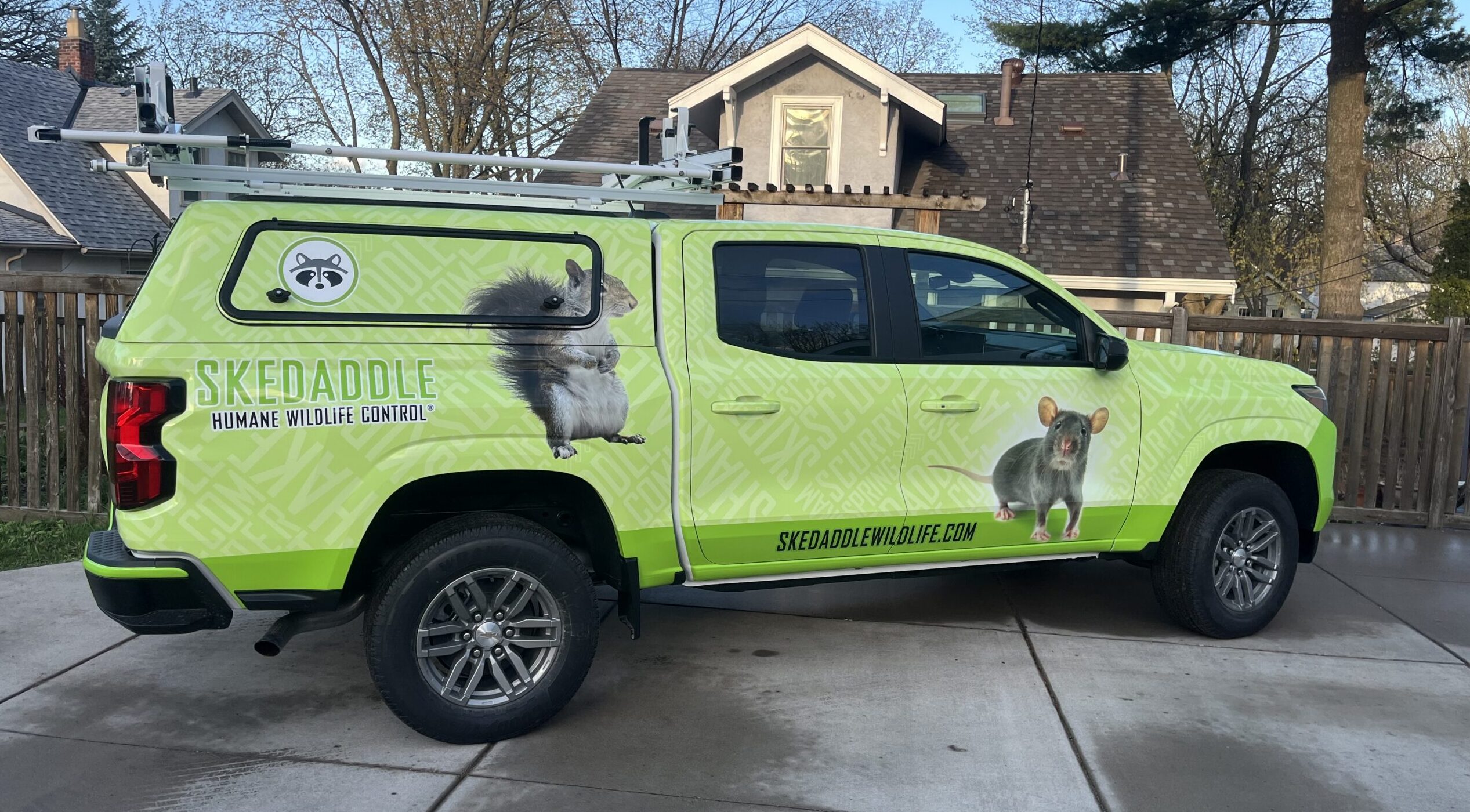 A bright green Skedaddle service truck with raccoon and squirrel graphics parked on a residential street in Minnesota.