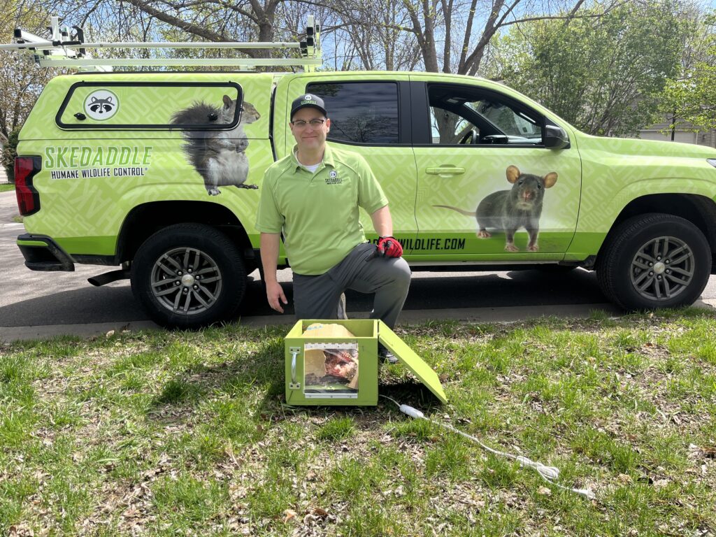 A Skedaddle technician in a green uniform kneeling next to a heated baby reunion box in front of a branded green service truck.