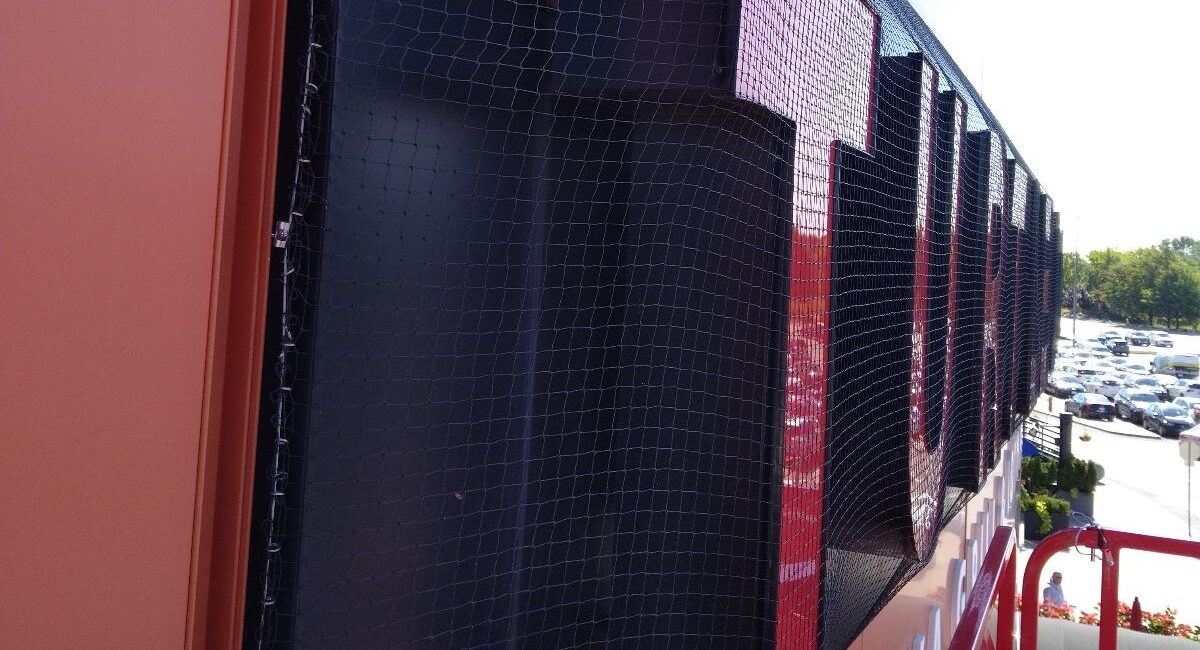 Close-up of black professional bird netting installed over large red and black commercial building signage to prevent pigeons from nesting.