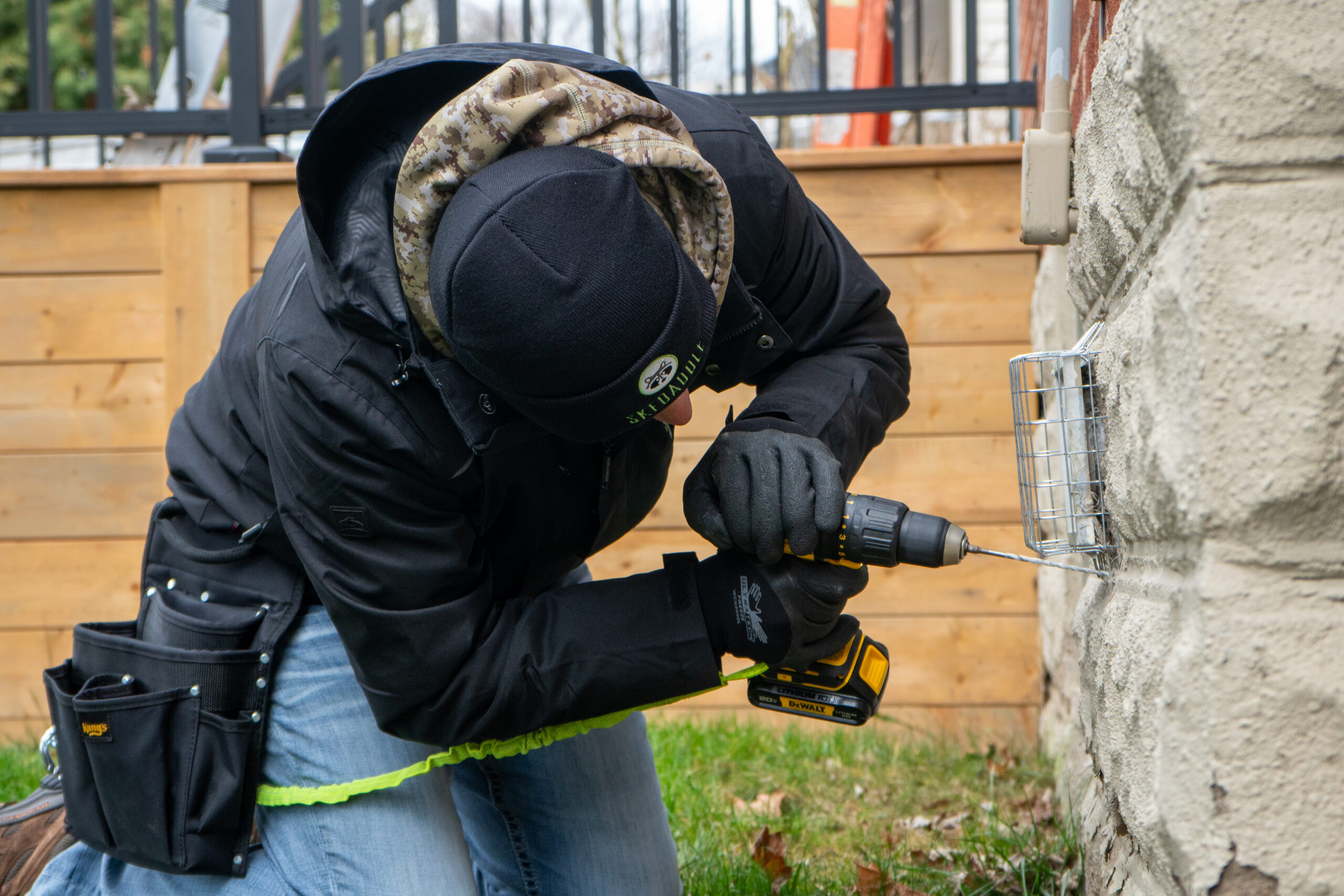 A Skedaddle wildlife technician using a power drill to install a heavy-duty mesh exclusion screen over an exterior wall vent.
