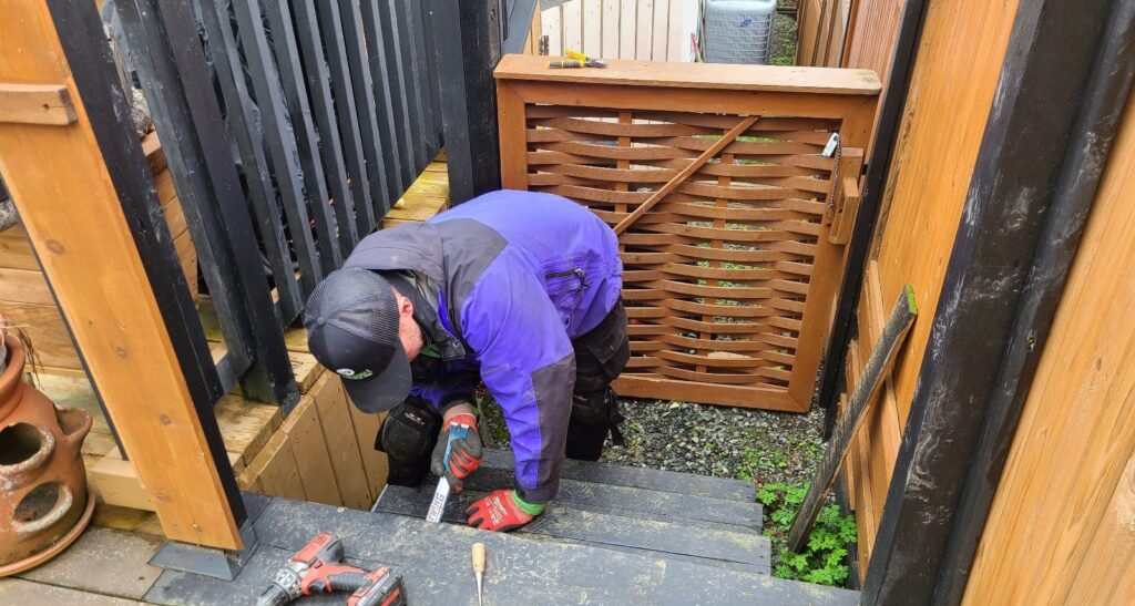 A Skedaddle wildlife technician using hand tools to install exclusion screening and seal entry points under a residential wooden deck.