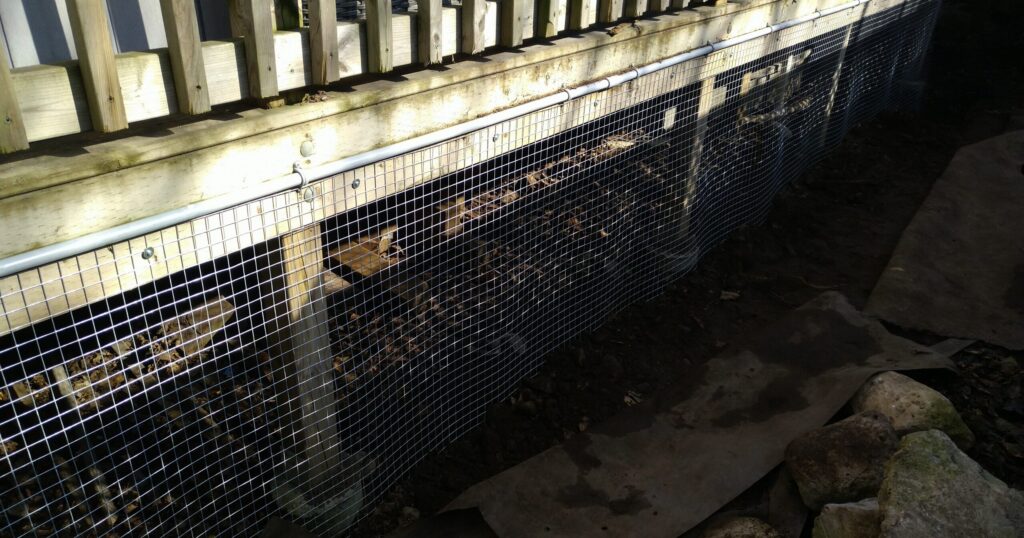 Heavy duty mesh screen installed under wooden deck A long section of galvanized steel mesh screening secured along the bottom of a wooden deck to prevent wildlife from burrowing underneath.