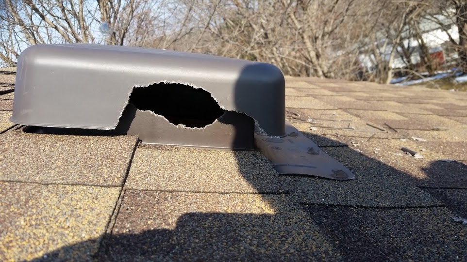 A close-up shot of a brown plastic roof vent on a shingled residential roof with a large hole chewed through the side by wildlife.
