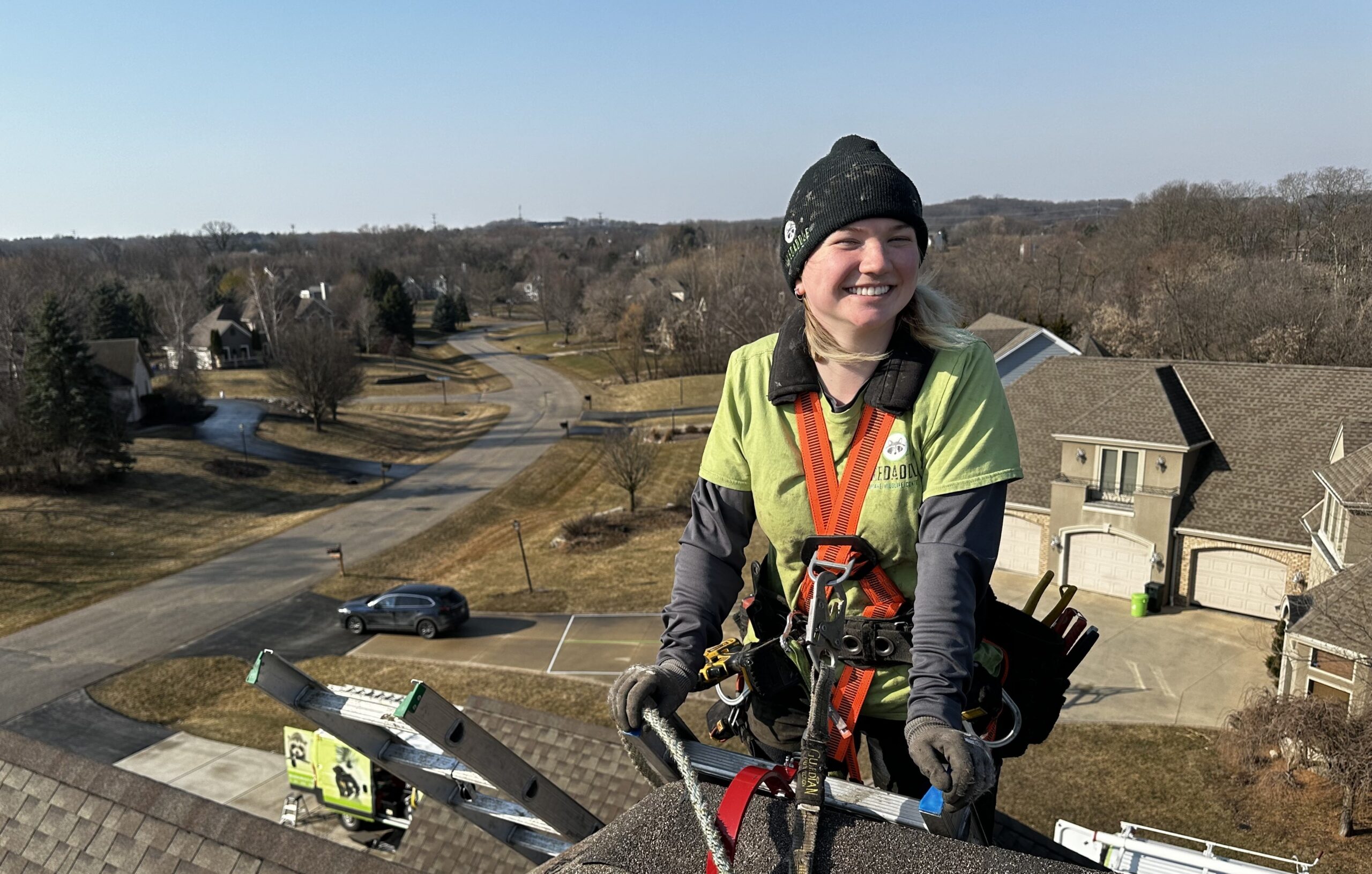 Skedaddle Technician on a full body harness and smiling in the roof