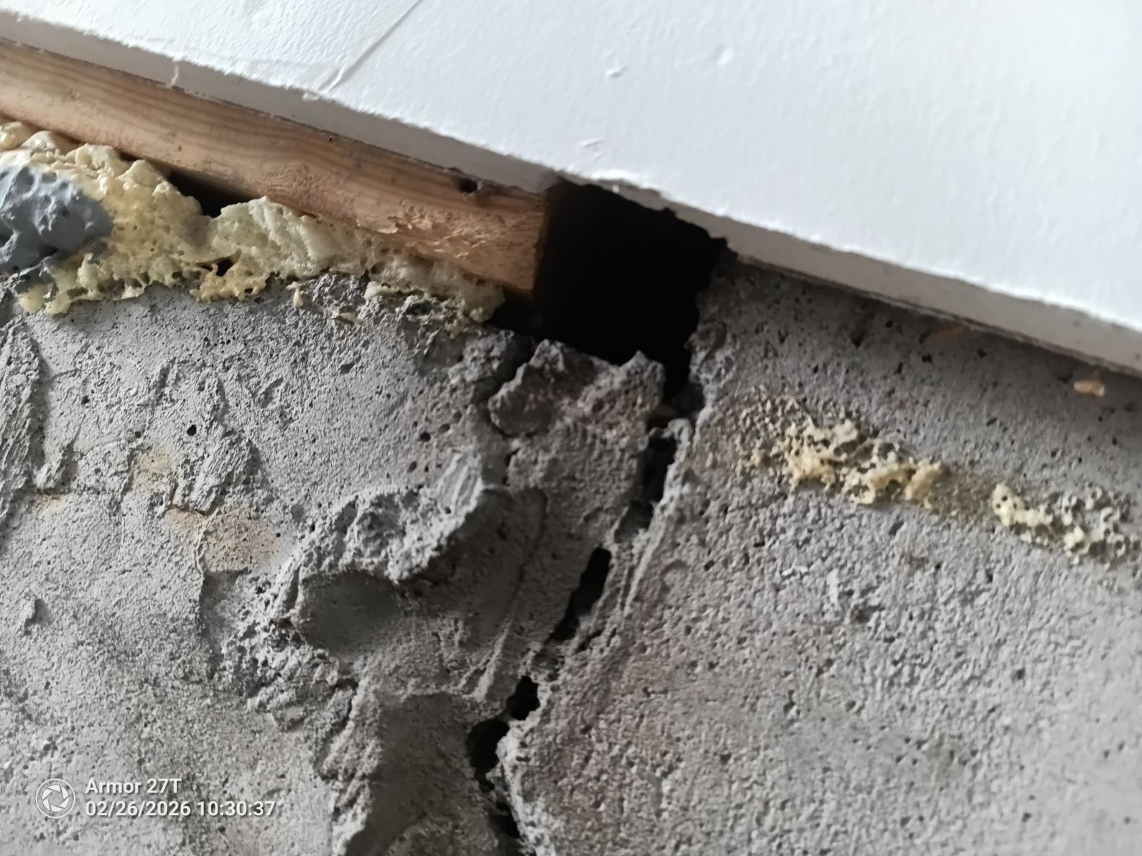 A close-up of a large structural gap and deep crack in a concrete foundation wall leading directly into a home's sill plate and floor framing.