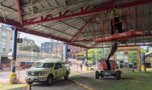 A lime green Skedaddle Wildlife service truck and a technician in a Skyjack boom lift working under a commercial canopy
