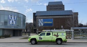 A lime green Skedaddle Humane Wildlife Control service truck parked in front of the University of Windsor campus