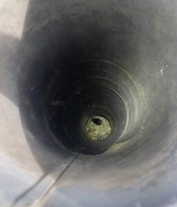 Looking down inside a long black plastic vent pipe where a small dark bird is visible at the bottom