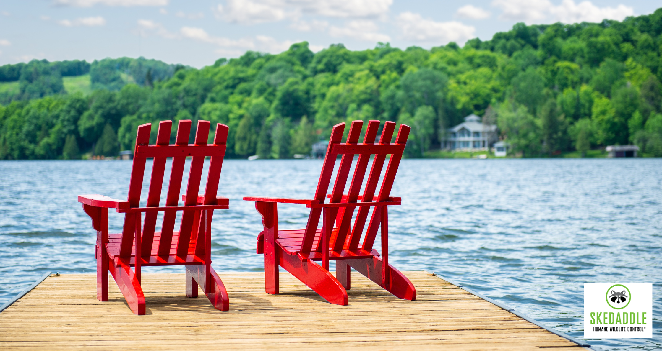 Two red Adirondack chairs on a wooden dock overlooking a lake with forested hills in the background