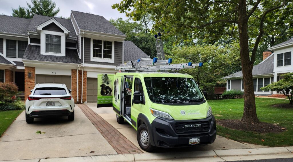 A bright green Skedaddle Humane Wildlife Control work van parked in a paved suburban driveway beside a two-story home