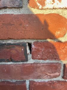 A narrow gap and void in the vertical mortar joint between red exterior bricks