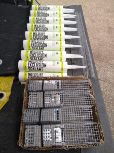 Tubes of wildlife exclusion sealant laid out next to a box of wire one-way exclusion doors and formed mesh strips